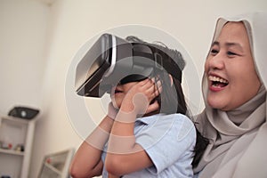 Happy cheerfull Asian muslim mother and daughter playing games on vr glasses