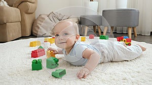 Happy cheerfull baby boy lying on floor next to colroful toys, bricks and blocks at playroom. Concept of children