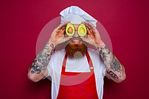 happy chef with beard and red apron holds an avocado