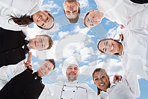 Happy chef and waiters standing in huddle against sky photo
