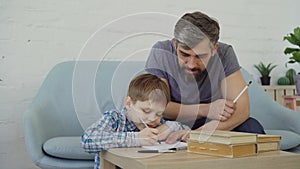 Happy child assiduous schoolboy is doing homework and talking to his father, little boy is learning and dad is teaching