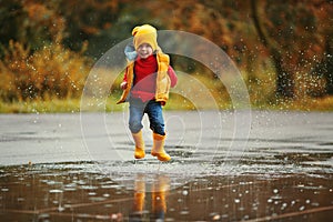 Happy child baby boy with rubber boots jump in puddle on autumn