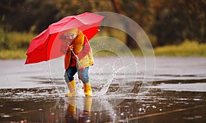 happy child baby boy with rubber boots and umbrella jump in puddle on autumn walk
