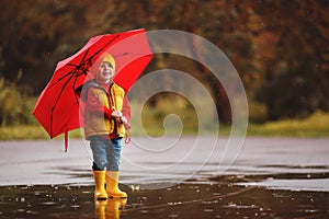 happy child baby boy with rubber boots and umbrella jump in puddle on autumn walk