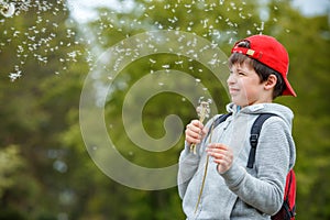 Happy child blowing dandelion flower outdoors. Boy having fun in spring park. Blurred green background