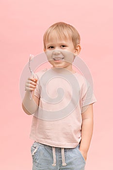 Happy child boy blond European appearance holding a toothbrush in his hands on a pink background
