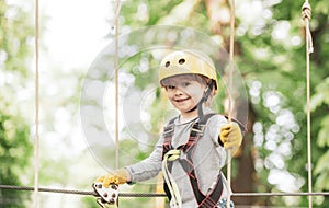 Happy child boy calling while climbing high tree and ropes. Portrait of a beautiful kid on a rope park among trees