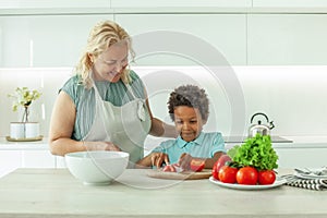 Happy child boy cooking a meal in kitchen watched over by his laughing mother