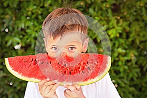 Happy child boy is eating a red juicy watermelon. Caucasian kid smiling and having fun. Concept of healthy food.