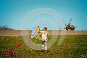 Happy child boy playing with a kite on meadow in summer in nature. Kid running on green field with colorful kite