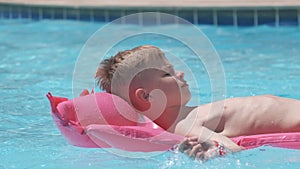 Happy child boy relaxing on inflatable air mattress in swimming pool on sunny summer day during tropical vacations