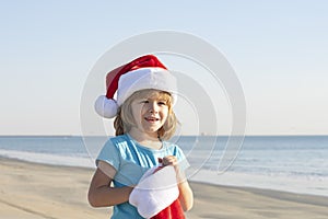 Happy child boy in Santa Claus hat on sea beach. School boy on winter vacation near sea. Happy Xmas and New Year holiday