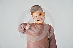 Happy child boy shows thumbs up and smiles on white background. Handsome kid posing and smiling.