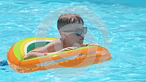 Happy child boy swimming on inflatable circle in swimming pool on sunny summer day during tropical vacations