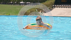 Happy child boy swimming on inflatable circle in swimming pool on sunny summer day during tropical vacations