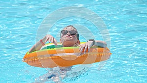 Happy child boy swimming on inflatable circle in swimming pool on sunny summer day during tropical vacations