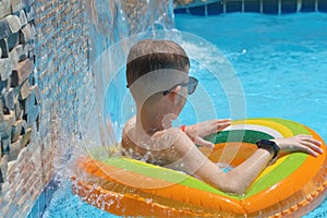 Happy child boy swimming on inflatable circle in swimming pool on sunny summer day during tropical vacations