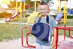 happy child with broken limb arm outdoors on playground background. school boy had accident on summer vacation. kid in a