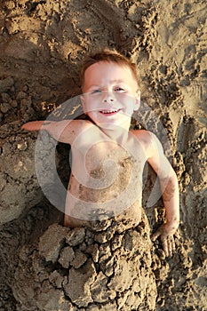 Happy child buried in sand on beach