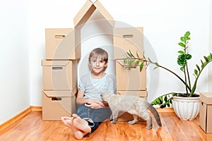 Happy child and cat having fun together at moving day in new home. Cute kid helping unpacking boxes