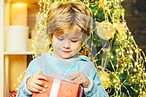 Happy child with Christmas gift. Portrait of Santa kid with gift looking at camera. Kid having fun near Christmas tree