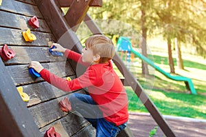 Happy child climbing on the wooden wall. Happy summer vacation. Kids outdoors playground