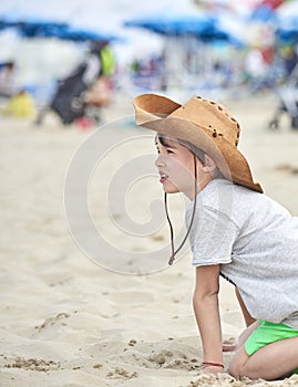 Happy child with a cowboy leather hat playing with sand..Close-up of a smiling child with cowboy hat, at the beach by the sea