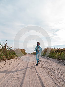 Happy child in denim jacket running jumping having fun on empty autumn sea beach. Blond girl walking on white sand road