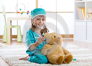 Happy child doctor girl examines teddy bear in nursery room at home.