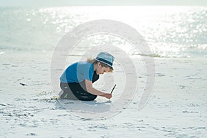 Happy child drawing on a sand in the summer sea. Kid having fun at the beach. Summer vacation and kids active. Travel