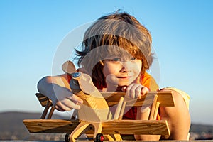 Happy child dreams of traveling and playing with toy airplane. Little pilot aviator in outdoor against blue summer sky