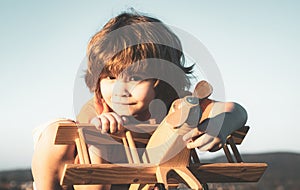 Happy child dreams of traveling and playing with toy airplane. Little pilot aviator in outdoor against blue summer sky