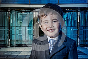 Happy child dressed businessman with hands in his tie and skyscrapers in the background