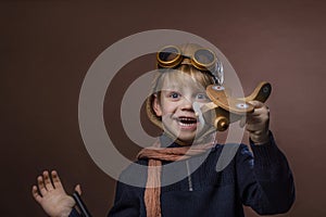 Happy child dressed in pilot hat and glasses. Kid playing with wooden toy airplane. Dream and freedom concept. Retro toned