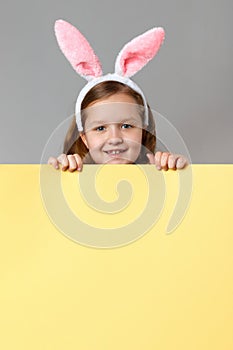 Happy child in easter bunny ears holding blank banner space on gray and yellow background