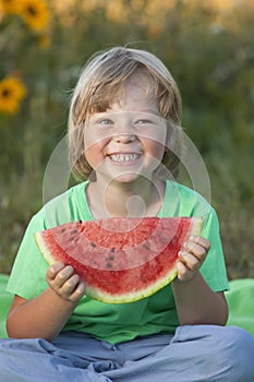 Happy child eating watermelon in garden. Boy with fruit outdoors