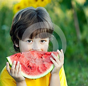 Happy child eating watermelon in garden. Boy with fruit outdoors park