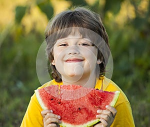 Happy child eating watermelon in garden. Boy with fruit outdoors park