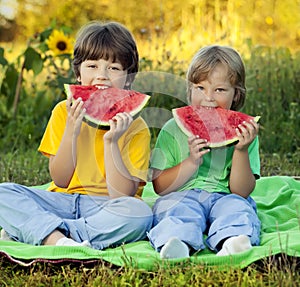 Happy child eating watermelon in garden. Two boys with fruit in