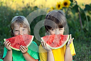 Happy child eating watermelon in garden. Two boys with fruit in