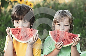 Happy child eating watermelon in garden. Two boys with fruit in park