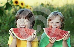 Happy child eating watermelon in garden. Two boys with fruit in park