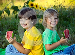 Happy child eating watermelon in garden. Two boys with fruit in park