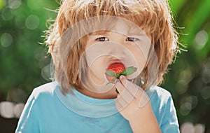 Happy child eats strawberries in the summer outdoor on green spring background. Close up kids happy face.