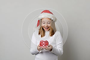 Happy child enjoying Christmas gift. Young girl in Santa hat with red Xmas present box on white background