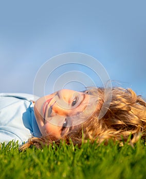 Happy child enjoying on grass field and dreaming. Kid relax on nature. Copy space on blue sky. Close up portrait of