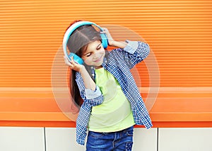 Happy child enjoys listens to music in headphones over colorful orange