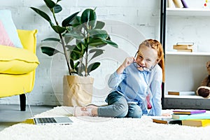 happy child in eyeglasses smiling at camera while studying with books and laptop