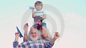 Happy child with father and grandfather playing with toy paper airplane against summer sky background. Grandfather