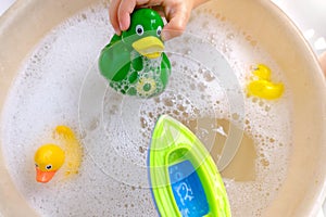 Happy child, girl 3 years old plays with rubber green, yellow ducks for swimming, plastic boat, child`s toys in soapy foam,